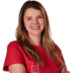 Uśmiechnięta higienistka stomatologiczna Katarzyna Banak w czerwonym fartuchu.